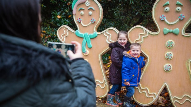 Two Children in winter clothing stood next to two large cut our ginger bread men, decorated with fake icing and sweets.